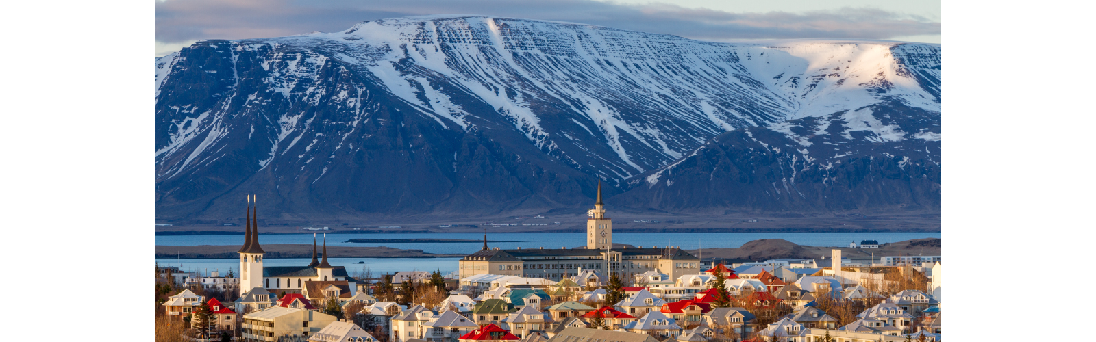A town with colorful roofs surrounded by mountains is bathed in sunlight. A tall spire of a cathedral stands out in the middle of the town. 